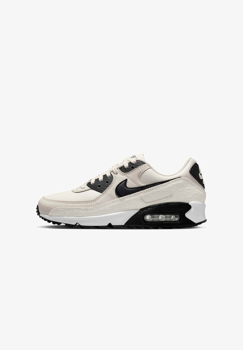 Baskets Nike Air Max blanches et noires avec semelle à coussin d'air visible, design à lacets et logo Nike swoosh noir sur le côté.