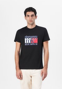 T-shirt en coton noir avec un design de logo coloré où "tommy" est écrit en accents blancs et rouges, à manches courtes et à col rond.