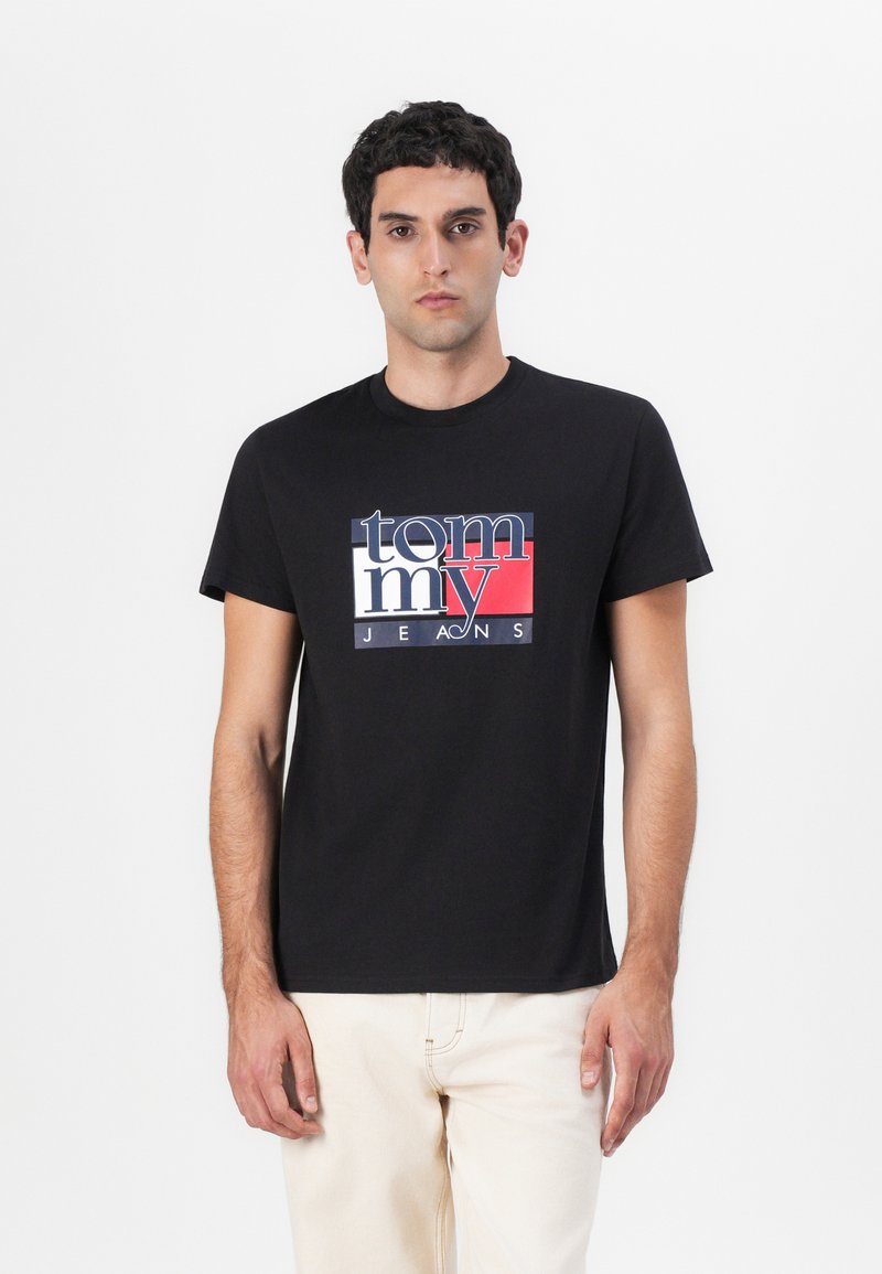 T-shirt en coton noir avec un design de logo coloré où "tommy" est écrit en accents blancs et rouges, à manches courtes et à col rond.