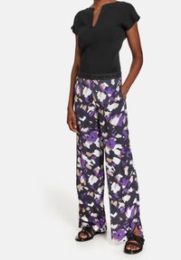 Haut noir à manches courtes avec un décolleté en V et un pantalon violet à motifs avec jambes larges et ceinture élastique contrastante. Sandales noires à brides.