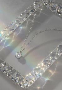 Sølv kæde halskæde med en rund, brilliant-slebet klar stenvedhæng, præsenteret på en reflekterende overflade med en prismelignende ramme.