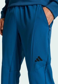 Blaue Sporthose aus glattem, leichtem Stoff. Verfügt über eine Reißverschlusstasche und ein schwarzes Logo am unteren Bein.