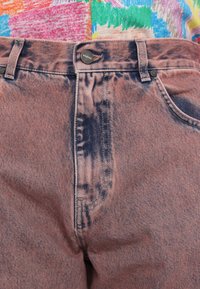 Un jean en denim rose présente une taille haute, des bandes plus foncées contrastantes, des poches standard et des détails en métal au niveau de la taille.