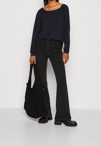 Navy long-sleeve top, black flared jeans, chunky black boots, and a textured black tote bag. Simple, casual outfit with layered textures.