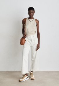 Beige ärmelloses Oberteil, hochgeschnittene weiße weit geschnittene Jeans, braune Umhängetasche und cremefarbene Sneakers mit tanfarbenen Akzenten. Einfaches Design, lässiger Look.