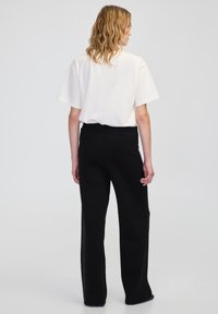 Weißes kurzärmliges Hemd mit lockerem Schnitt, kombiniert mit hochgeschnittenen schwarzen weiter geschnittenen Hosen, die eine glatte Textur und keine sichtbaren Muster aufweisen.