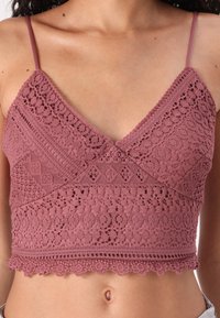 Lace crop topp i mauve med justerbare stropper, med intrikate mønstre og bølgete kanter. Myk tekstur med lagdelt detaljering.