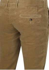 Bruine corduroy broek met achterzak met knoop, riemlussen en zichtbare verticale geribbelde textuur.