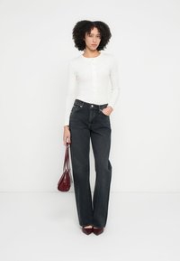 Bílý top s dlouhým rukávem a zapínáním na knoflíky, tmavé džínové džíny s vysokým pasem a rozšířeným střihem, bordó kabelka a boty na podpatku se špičatou špičkou. Minimalistický design.