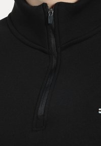 Acercamiento a un collar de prenda negra con cremallera que está parcialmente cerrada, mostrando detalles de costura visibles.