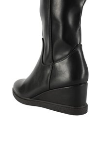 Stivaletto nero con zeppa alla caviglia, finitura in pelle liscia, punta arrotondata e suola in gomma testurizzata. Presenta un design con ritaglio laterale.