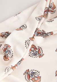 Tissu crème avec plis présentant un motif floral répété dans des tons bleu atténué, rouille et beige.