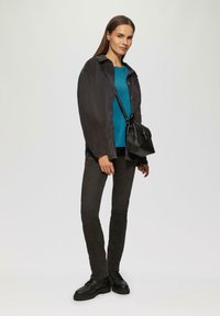 Zwarte jas, teal top, grijze broek en zwarte laarzen; gecombineerd met een kleine zwarte schoudertas; strakke lijnen en eenvoudig ontwerp.