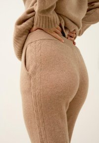 Beżowy sweter z dzianiny i dopasowane spodnie z teksturowanym wzorem kablowym po bokach, wykonane z miękkiego materiału przypominającego wełnę.