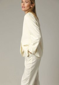 Crème-kleurig op maat gemaakt jasje met een relaxte pasvorm, met lange mouwen en zijzakken, gecombineerd met bijpassende broek. Gladde textuur.