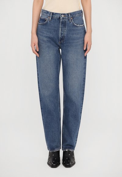 Jean en denim bleu avec une coupe décontractée, taille haute, design à cinq poches, lavage délavé et ourlet effiloché, associés à des bottes noires à bout pointu.