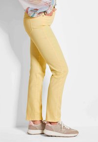 Gelbe Denim-Hosen mit geradem Bein und Seitentaschen, kombiniert mit beigen und rosa Sportschuhen mit strukturiertem Design und Schnürsenkeln.