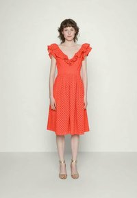 Vestido vermelho com bolinhas, decote e mangas com babados. Silhueta em A com cintura ajustada, comprimento até o joelho e tecido texturizado.