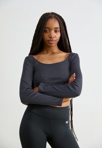 Long-sleeve, dark gray ribbed top with a wide neck. Model wearing black high-waisted leggings with a small logo on the waistband.