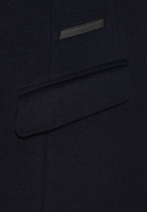 Granatowy płaszcz z wełny z elegancką, płaską kieszenią z czarnym wykończeniem oraz subtelnym brązowym przeszyciem.