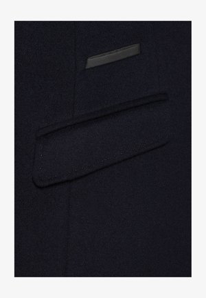 Granatowy płaszcz z wełny z elegancką, płaską kieszenią z czarnym wykończeniem oraz subtelnym brązowym przeszyciem.