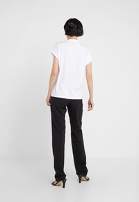 Camisa polo blanca de mangas cortas combinada con pantalones negros de corte recto y sandalias de tacón alto negras, vista desde atrás.