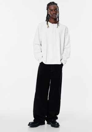 Witte lange mouwen henley-shirt met drie knopen, gecombineerd met zwarte wijde corduroy-broek en zwarte laarzen met dikke zool.