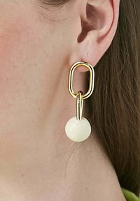 Guldörhängen med en avlång oval länk och en slät, vit sfärisk accent längst ner. Elegant och modern design.