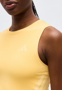 Κοντινό πλάνο ενός ατόμου που φοράει κίτρινο αθλητικό αμάνικο τοπ με διακριτικές οριζόντιες ρίγες στο στήθος και την πλευρά.