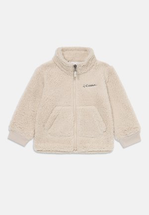 Veste en polaire beige clair avec col haut, fermeture éclair à l'avant, deux poches et poignets côtelés, arborant le logo Columbia en haut à gauche.