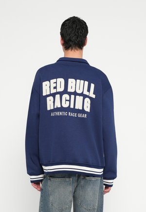 Marineblå sweatshirt med hvid "RED BULL RACING" tekst, ribbet manchetter og kant, lavet af blødt materiale, med en afslappet pasform og krave.