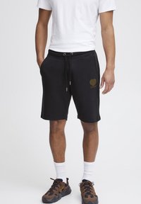 Pantalones cortos de algodón negros con cinturilla elástica, cierre con cordón, bolsillos laterales y un gráfico de corazón en dorado en la pierna izquierda.
