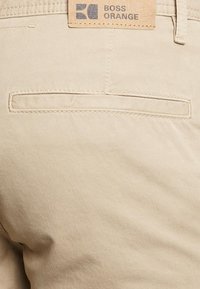 Beiga bomullbyxor med en slät textur, med en bakficka och en läderetikett med "BOSS ORANGE"-logotypen.