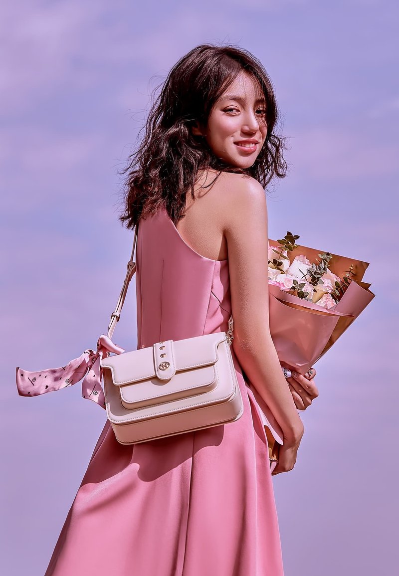 Borsa rosa con un design strutturato, accessori in oro e una sciarpa a motivo staccabile. Bouquet floreale lussureggiante in mano.