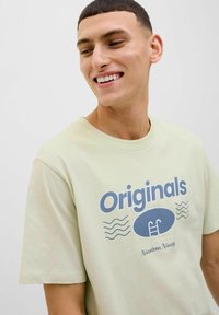 Lichtgroene katoenen t-shirt met een ronde hals. Centraal grafische tekst "Originals" in het blauw, met golfpatronen en een ovale vorm eronder.