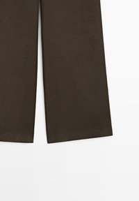 Bruine broek met wijde pijpen en een nette zoom, plat liggend op een witte achtergrond.