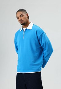 Blauwe zip-up trui met een witte kraag, losse pasvorm, lange mouwen en een gladde textuur, gecombineerd met donkere spijkerbroek.