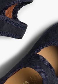 Zapatos planos de ante azul marino con un forro interior suave, que presentan un borde con forma de ondas y acentos elásticos en las aberturas para facilitar su uso.