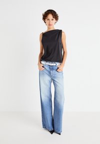 Haut sans manches noir avec un design drapé, associé à un pantalon large bleu clair. La tenue comprend une ceinture en argent et des chaussures noires pointues.