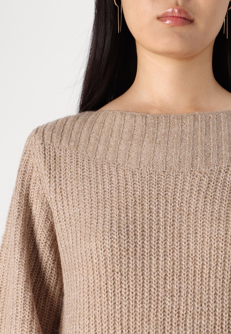 Beiger Strickpullover mit weitem Bootsausschnitt, ausgestattet mit einer gerippten Textur und lockeren Ärmeln, die ein weiches, gemütliches Erscheinungsbild betonen.