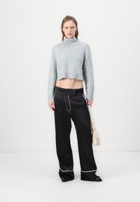 Un pull court gris clair avec col roulé, associé à un pantalon large noir avec des accents rouges et un ourlet blanc, tenu avec un sac beige.