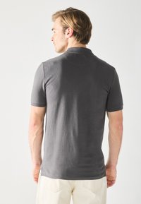 Gray short-sleeve polo shirt with a textured fabric. Features a classic collar and side slits, paired with light-colored trousers.