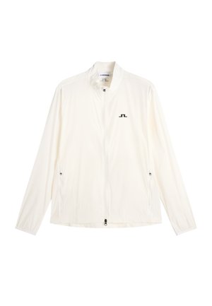 Valkoinen kevyt takki, jossa on täysi vetoketju edessä, sivuvetoketjulliset taskut, joustavat resorit hihoissa ja pieni musta logo vasemmassa rinnassa.