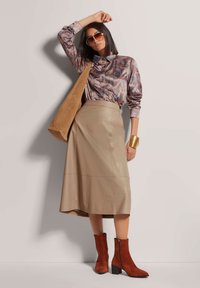 Glanzend gedessineerd shirt met lange mouwen, beige leren rok, bruine suède enkellaarsjes met blokhakken, en een tan schoudertas.