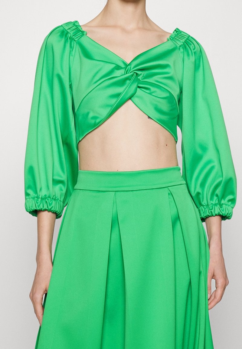 Crop top en satin vert avec devant torsadé et manches trois-quarts bouffantes, associé à une jupe plissée verte taille haute.