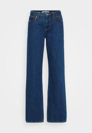Jeans de mezclilla azul acampanados con costuras de contraste, diseño de cinco bolsillos y cierre de cremallera. La tela tiene una textura suave con ligero desgaste.