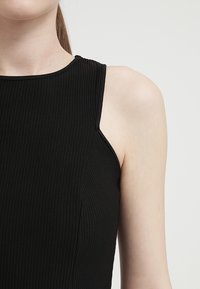 Top negro de canalé con escote alto y diseño sin mangas, que presenta un ajuste ceñido y una sutil textura en una tela suave.