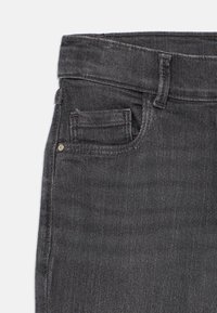 Jeans de denim cinza escuro com um bolso frontal, detalhes costurados e uma cintura de altura média. Textura suave com um brilho subtil.