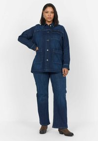 Jeans jakna in ujemajoči se temno modri jeans. Jakna ima dve sprednji žepki, gumbasto zapiranje in ovratni izrez. Gladka tekstura.