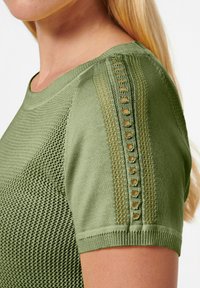 Grünes Strickoberteil mit kurzen Ärmeln, strukturiertem Muster auf dem Oberkörper und dekorativen offenen Details entlang der Schulternähte.